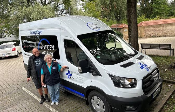 Weißer Kleinbus für die Tagespflege mit zwei Personen daneben