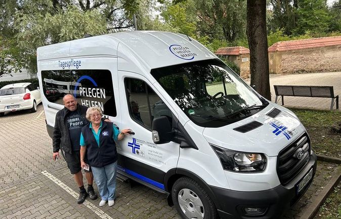 Weißer Kleinbus für die Tagespflege mit zwei Personen daneben